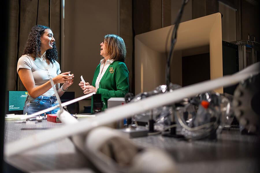 A student and a professor talk in lab with an airplane model in the foreground