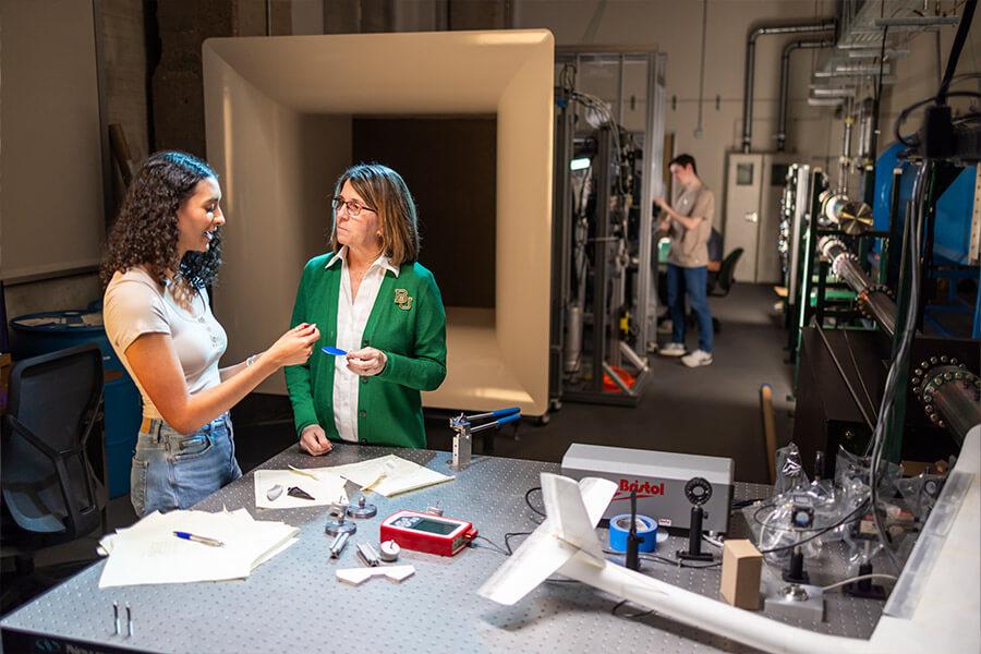 A student and a professor talk in lab with an airplane model on the table